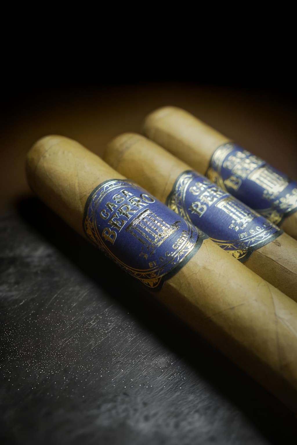 Three Casa Berro Blue cigars on dark slate, low key lighting.